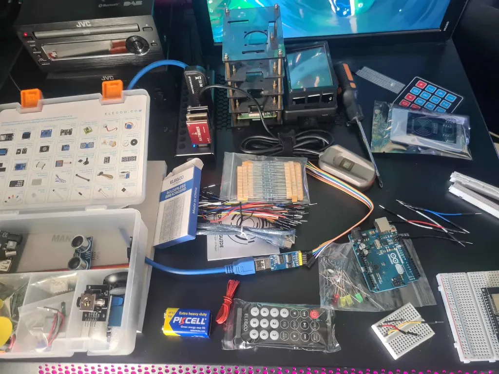 Electronics components spread across a workbench, including an Arduino, breadboards, jumper wires and resistors