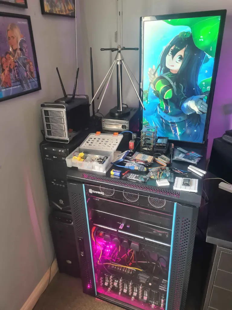 Electronics workbench above a lit server rack with parts, tools and a vertical monitor