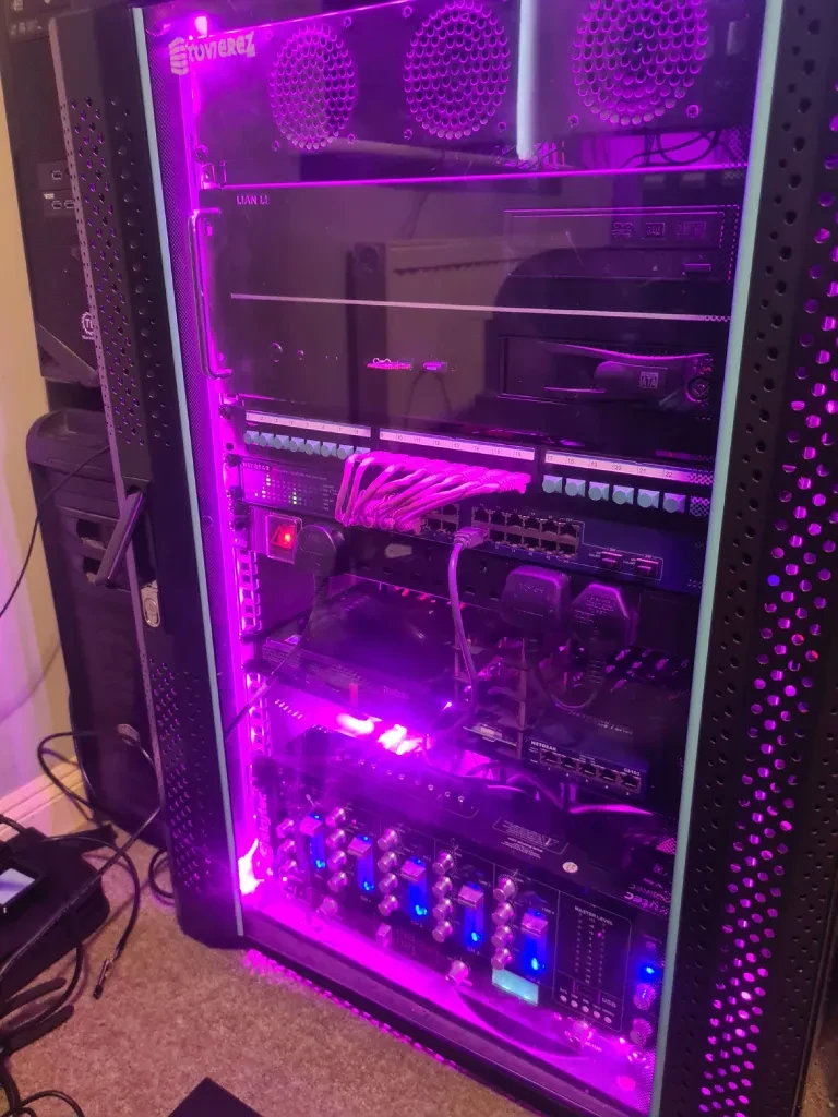 Home lab rack filled with network and computer hardware under purple lighting