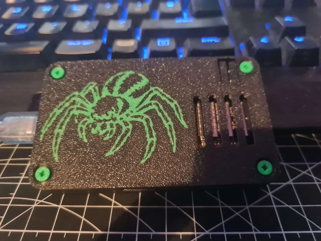 Black electronics case with a green spider design, green screws and ventilation slots